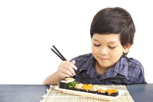 menino adorável asiático está comendo sushi isolado sobre fundo branco foto