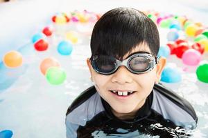 menino brincando com bola colorida em brinquedo de piscina pequena - menino feliz no conceito de brinquedo de piscina de água foto