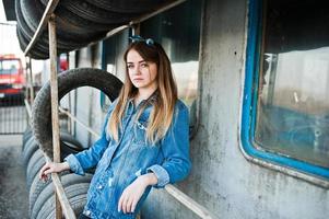 garota jovem hippie na jaqueta jeans e lenço na cabeça na zona de montagem do pneu. foto