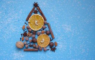 árvore de natal feita de avelãs, nozes, especiarias e fatias de laranja, neve de lascas de coco em um fundo azul. foto de alta qualidade