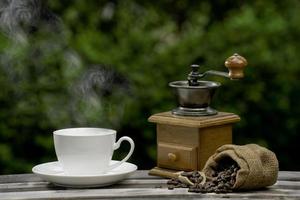 xícara de café com um moedor, grãos de café escuros no antigo piso de madeira, close-up de sementes de café em um fundo natural.