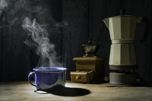 xícara de café esmaltada com fumaça. conjunto de café com bule de moka e moedor no antigo piso de madeira. foco suave.