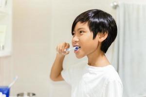 menino escovando os dentes com escova de dentes no banheiro. foto