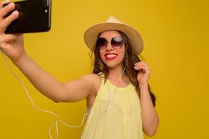 feche o retrato de uma mulher morena feliz na blusa amarela e chapéu fazendo selfie em fundo amarelo. foto