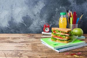 almoço saudável para a escola com sanduíche, maçã fresca e suco de laranja. material escolar colorido sortido. copie o espaço. foto