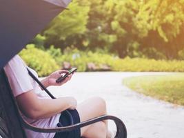 senhora relaxa sentado no parque com guarda-chuva e usando telefone celular foto