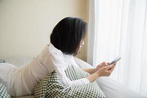 mulher usando telefone celular enquanto acorda na cama de manhã - tecnologia no conceito de vida cotidiana foto