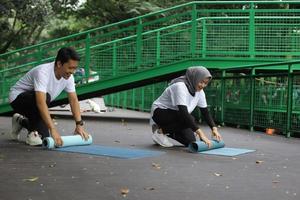 jovem casal asiático rolando esteira de pilates de ioga após workput no parque. conceito de casal de estilo de vida saudável. foto