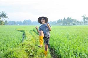 atraente jovem agricultor asiático alegre, regozijando-se por ter sucesso no cultivo de arroz em casca no campo de arroz. conceito de agricultura moderna. foto