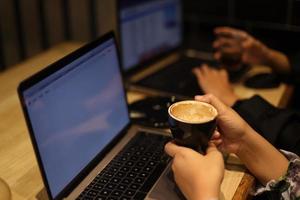 freelancer feminino trabalhando online no computador enquanto segura a caneca de café. conceito de rede e ocupação. foto