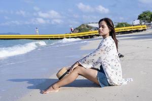 mulher preocupada sentada na praia com um chapéu de palha na praia tropical de joelhos à beira-mar no dia ensolarado. garota solitária sentada sozinha à beira-mar, relaxando e pensando. fotografia de conceito de emoção humana foto