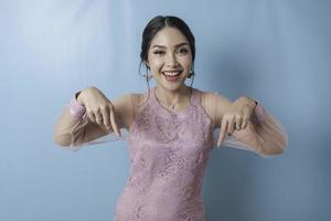 mulher asiática animada vestindo roupas modernas de kebaya apontando para o espaço da cópia para baixo foto