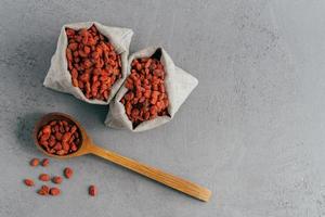 tiro isolado de bagas de goji vermelhas secas em dois pequenos sacos e na colher de sopa de madeira. vista do topo. superalimento com antioxidantes, minerais e vitaminas foto