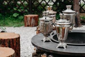 quatro samovars metálicos ao ar livre e tocos de madeira ao redor. ambiente acolhedor para beber chá. tempos antigos na rússia foto