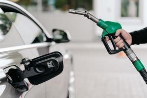 foto recortada da mão do homem bombeando gasolina no carro no posto de gasolina. auto sendo abastecido com gasolina. homem irreconhecível detém nozzel de combustível.