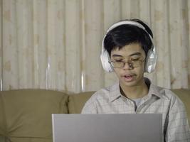 o menino usando fones de ouvido sentado à mesa com o professor do skype de bate-papo na internet se prepara para o exame e usa o laptop para sua lição de casa e e-learning para educação on-line. aprendendo o conceito de crianças. foto