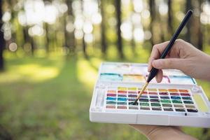 relaxe a mulher pintando o trabalho de arte da cor da água na natureza da floresta do jardim verde - pessoas com arte criativa na natureza redução do estresse e conceito de meditação foto