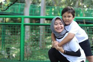 retrato de criança asiática abraça a mãe de volta, aproveitando o tempo em família no parque. unindo o conceito de família feliz. foto