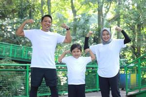 jovem mãe asiática e pai fazendo um gesto de braço forte junto com o filho no parque verde. conceito de família de estilo de vida saudável. foto