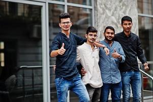 grupo de quatro homens indianos, use roupas casuais, posou ao ar livre na rua da índia. mostra o polegar para cima. foto