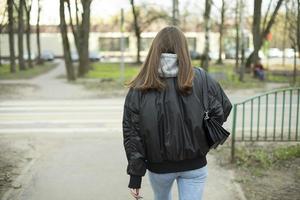 garota de jaqueta preta e jeans azul caminha pela rua. mulher caminha pela cidade. foto