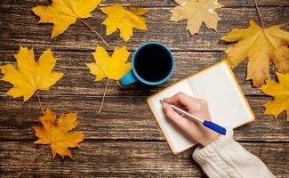 mão feminina escrevendo algo no caderno perto de xícara de café. foto