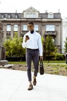 jovem empresário americano africano usando um telefone celular enquanto caminhava na rua aa