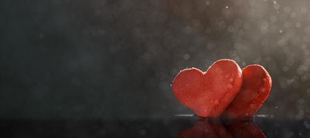 dois corações vermelhos com gotas de chuva iluminadas por luz quente sobre fundo escuro com um bokeh. foto com espaço de cópia.