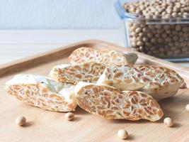 tempeh cru ou tempe. fatias de tempeh na placa de madeira e uma tigela de soja seca na mesa de madeira. tempeh é uma comida tradicional da Indonésia. foto