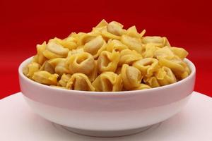 macarrão tortellini cru em uma tigela isolada em fundo vermelho. massa italiana tradicional foto