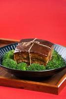carne de porco dong po em um prato azul com brócolis com fundo vermelho. foto