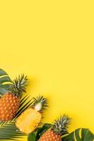 lindo abacaxi em folhas tropicais de palmeira monstera isoladas em fundo amarelo pastel brilhante, vista superior, postura plana, sobrecarga acima das frutas de verão. foto
