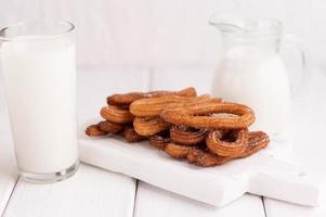 churros caseiros com leite e creme em um fundo branco de madeira. foto