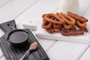 churros caseiros com chocolate em um fundo branco de madeira. foto