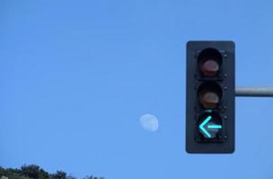 a seta de um semáforo apontando para a lua com céu azul ao redor foto