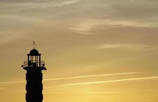 um farol se destaca contra o céu dourado durante um pôr do sol em lisboa, portugal foto