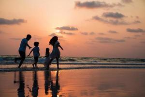 família silhueta andando e brincando no pôr do sol da praia com o conceito de férias felizes para crianças foto