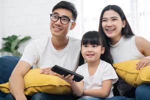 feliz família asiática passando tempo assistindo tv juntos no sofá na sala de estar. conceito de família e lar foto