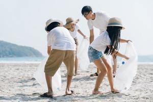 voluntário da família asiática pegando uma garrafa de plástico em uma praia com mar para proteger o meio ambiente foto