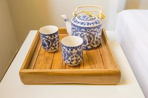 tradicional xícara branca de chá e bule na bandeja de madeira closeup na mesa foto