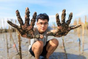 um jovem adolescente asiático mostrando as mãos sujas depois de plantar uma árvore com um rosto feliz e orgulhoso foto