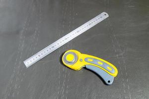 régua de aço e cortador rotativo na superfície de couro foto