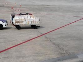 bagagem de serviço de solo bagagem e encomenda no carrinho de carrinho de carrinho entregando ao avião na pista de táxi com marcação de linha vermelha no aeroporto. foto