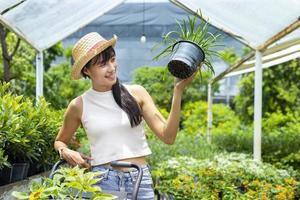 jovem cliente asiático está escolhendo plantas exóticas do viveiro do centro de jardinagem local com carrinho de compras cheio de plantas de verão para jardinagem de fim de semana e busca ao ar livre foto