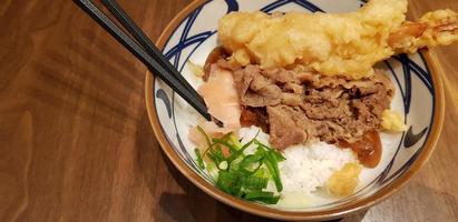 comida tradicional japonesa carne teriyaki com arroz stickt e camarão tempura cebolinha fatiada em uma tigela foto