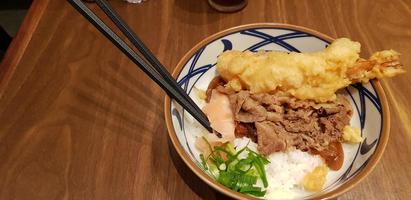 comida tradicional japonesa carne teriyaki com arroz stickt e camarão tempura cebolinha fatiada em uma tigela foto