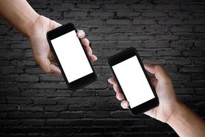 duas mãos segurando a tela em branco de um smartphone na velha parede de tijolos pretos. foto