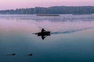 silhueta de homem em um barco no início da manhã. amanhecer rosa com patos foto