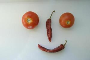tomates orgânicos maduros vermelhos e pimenta vermelha quente seca no peitoril da janela na forma de um smiley e emoji foto