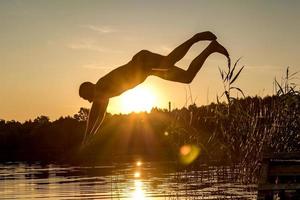 homem mergulha na água do lago ao pôr do sol foto